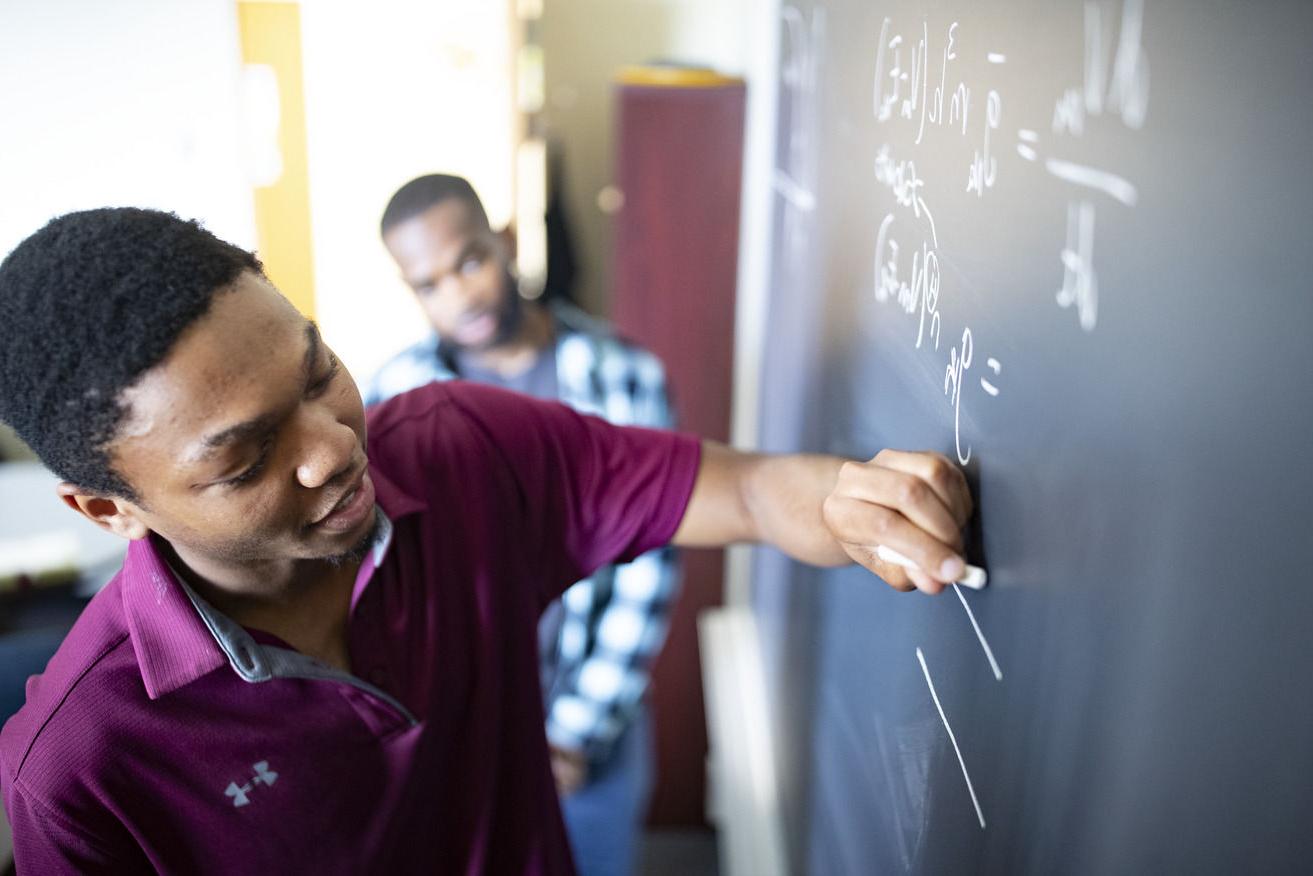 An image of a student writing a math equation on a chalkboard.