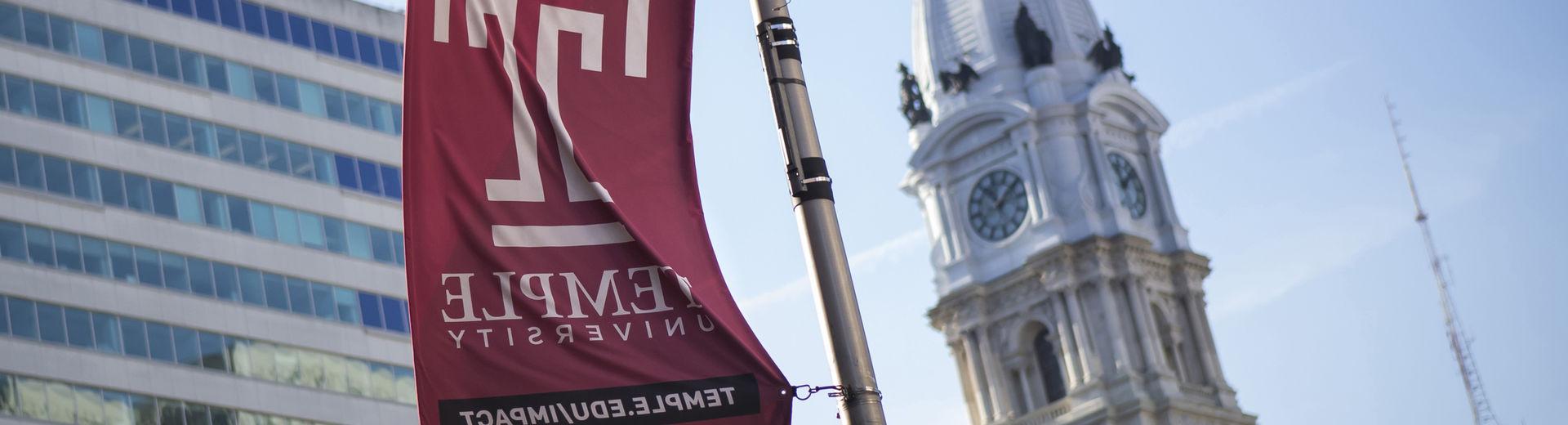 The Temple cherry T flag waves in front of the Philadelphia City Hall building