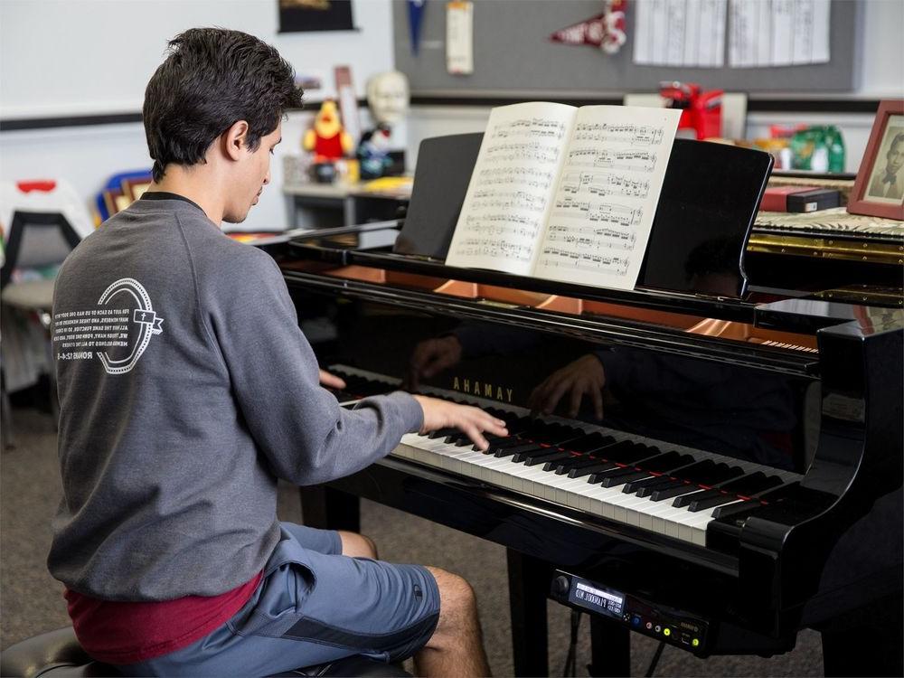 A male student plays a baby grand piano.