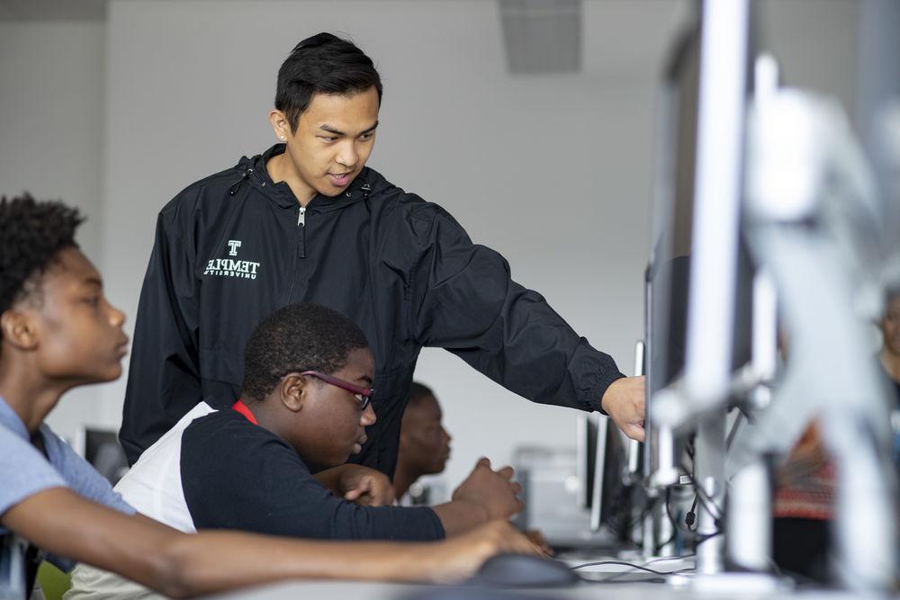 科技学院学生在台式电脑上指导中学生. 